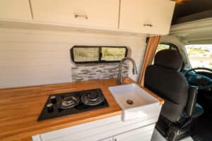 Teak countertop with stovetop and farm sink next to the swivel seat