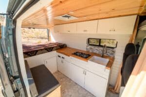 Interior of the 2019 Ram Promaster Bennett camper van from the sliding door: white cabinets, teak countertop and knotty pine ceiling