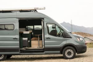 Side view of the Ford Transit 250 camper van with roof rack below mountains