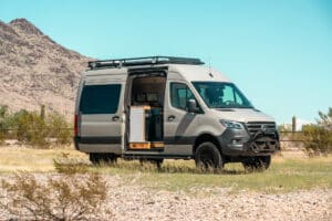 Side view of the 2024 Mercedes-Benz Sprinter Maddox camper van with roof rack and open sliding door in the Arizona desert