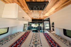 Bed made up across the rear of the van under the wood ceiling and MaxxAir fan