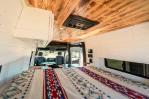 Bed with patterned blanket and overhead cabinets, looking forward to the cab
