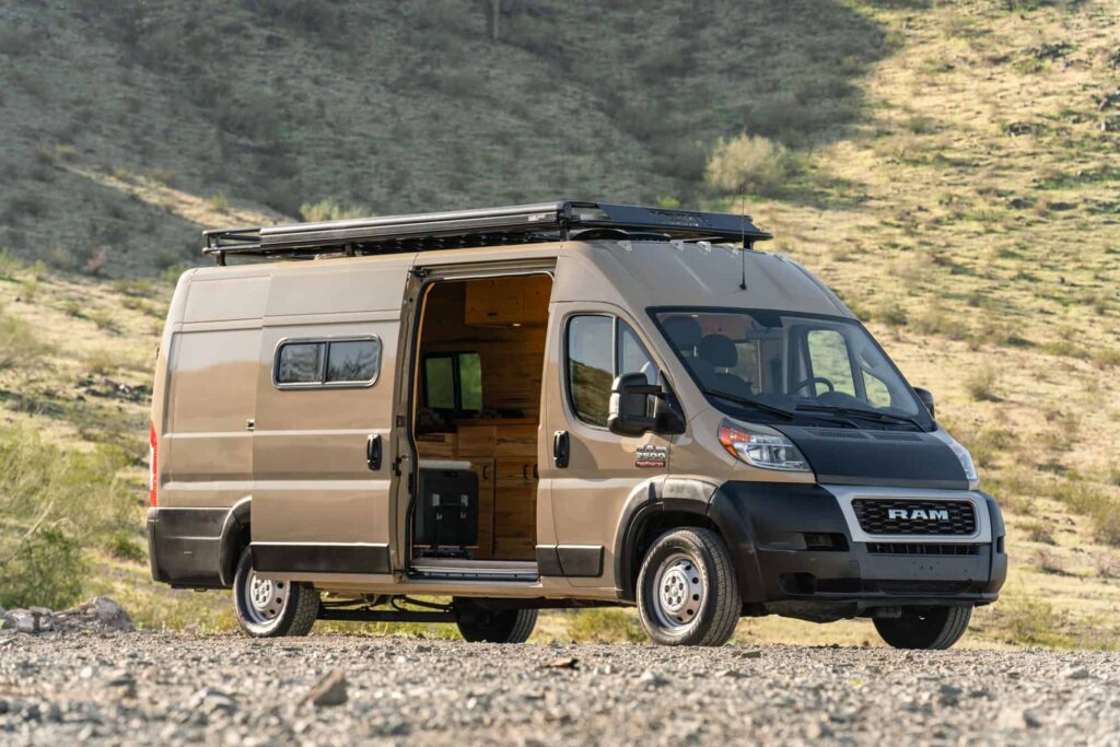 Front three-quarter view of the Desert Sand Ram ProMaster camper van with black RAM grille, roof rack and open sliding door