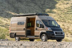 Front three-quarter view of the Desert Sand Ram ProMaster camper van with black RAM grille, roof rack and open sliding door